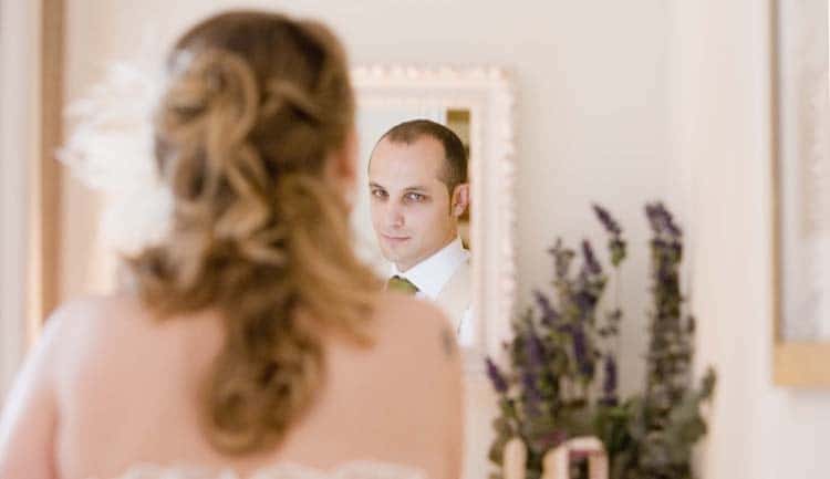 Novia maquillandose en un espejo donde se ve el reflejo del novio.
